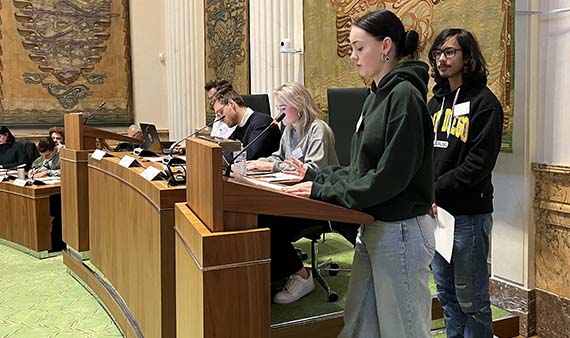 Priscilla en Noah achter het spreekgestoelte van de statenzaal tijdens het jongerendebat met Statenleden